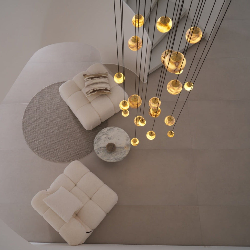 Bird's-eye view of the lit chandelier over a round rug, marble table and two cream boucle chairs.