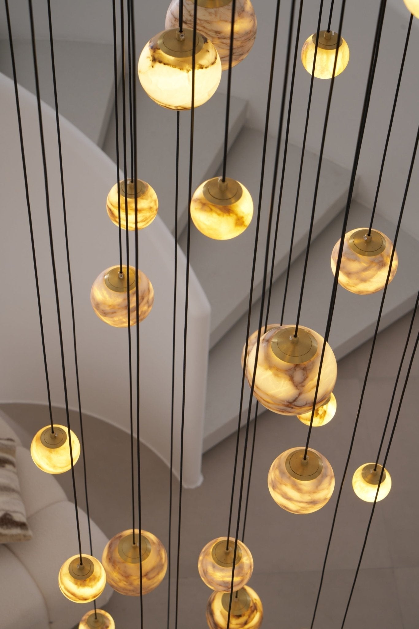 Upward view of the lit globes and their brass caps, cables running past the curve of the stair.