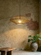 Beside an exposed brick wall and a terracotta planter, this Clérachic pendant casts a warm pool of light on weathered plaster.