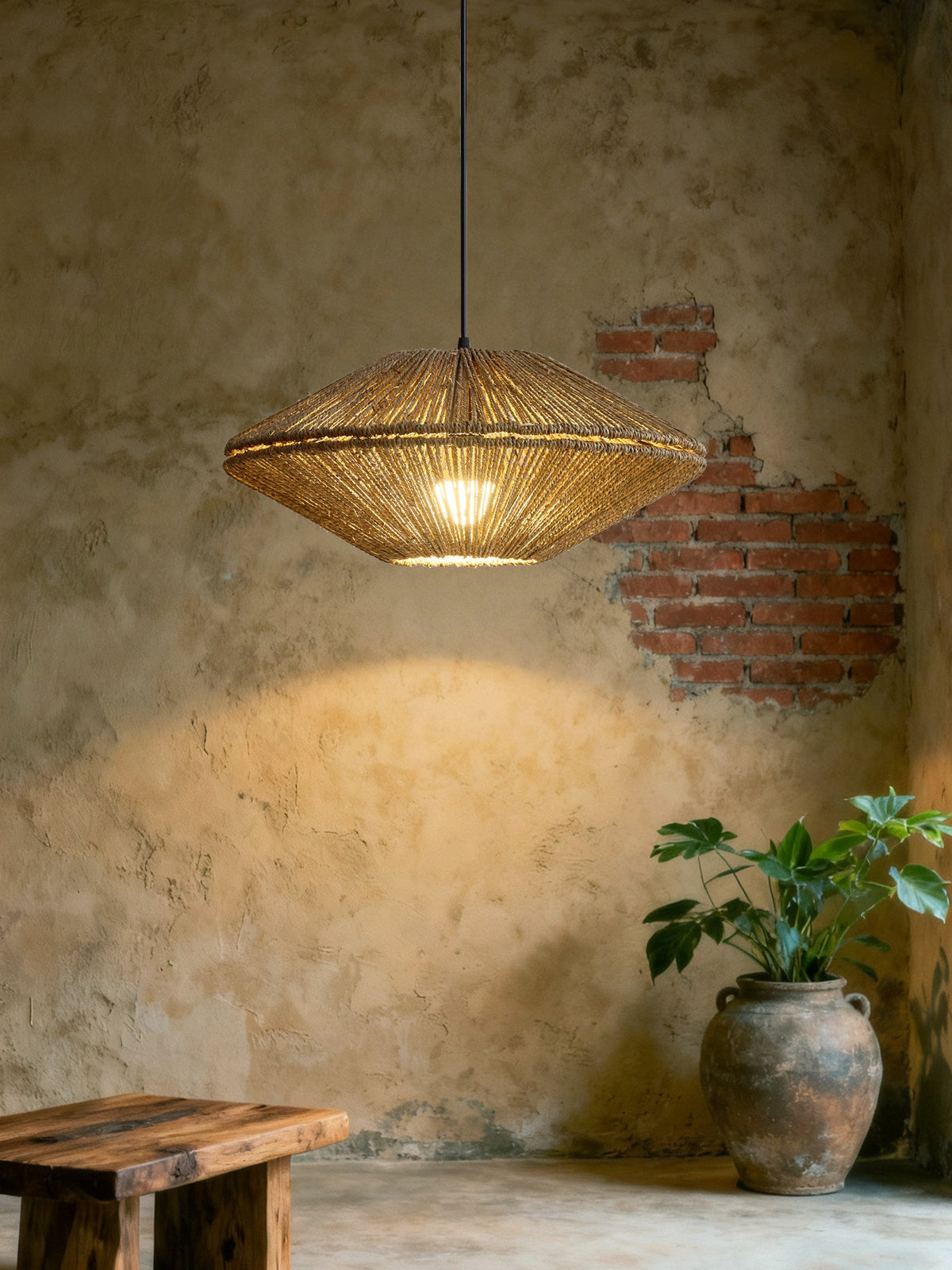 Beside an exposed brick wall and a terracotta planter, this Clérachic pendant casts a warm pool of light on weathered plaster.