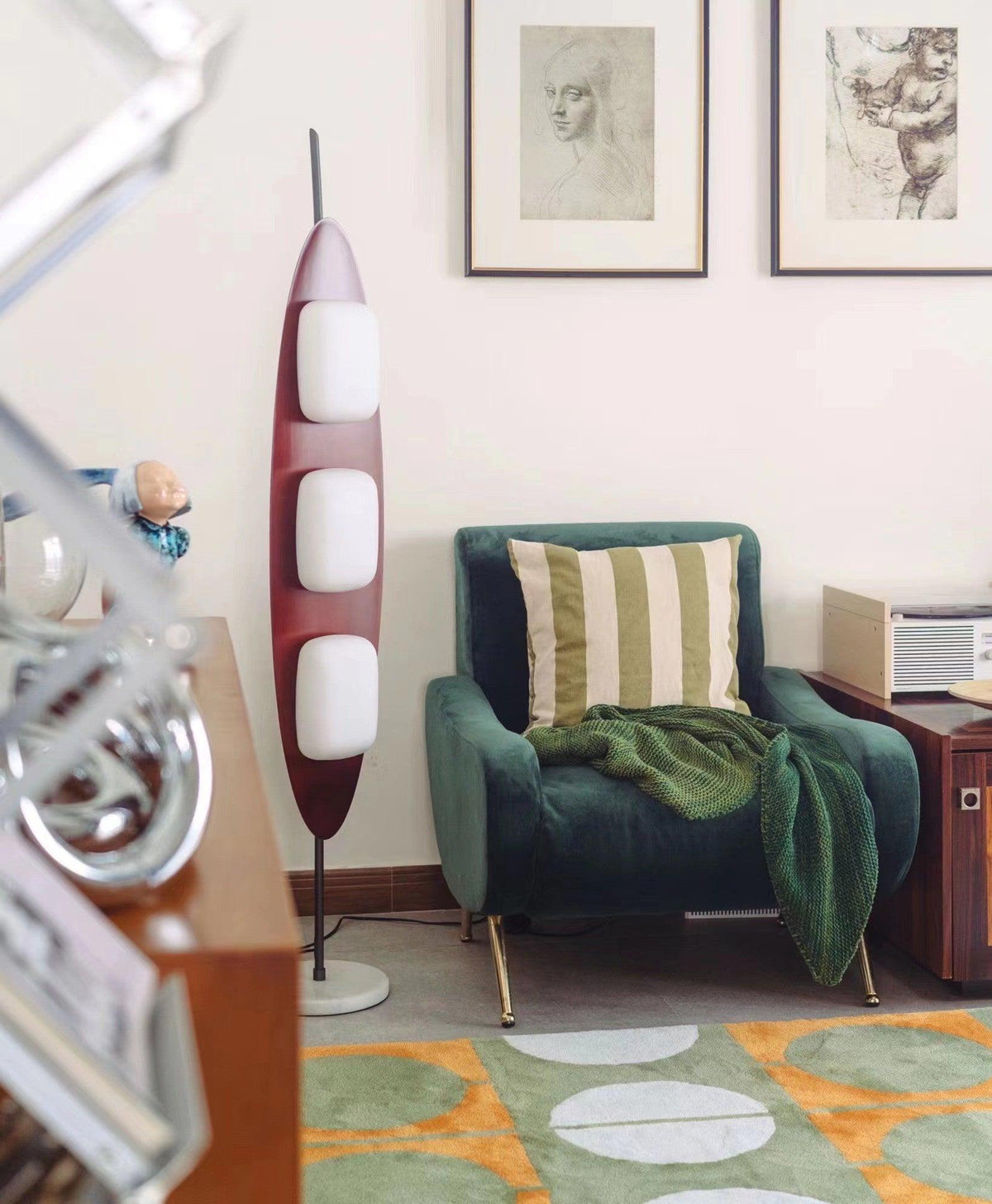 Clérachic teak floor lamp beside a striped green armchair and framed line-art prints in a colourfully rugged room.