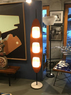 Clérachic teak floor lamp on display beside framed artwork and other lighting pieces in a gallery-style showroom setting.