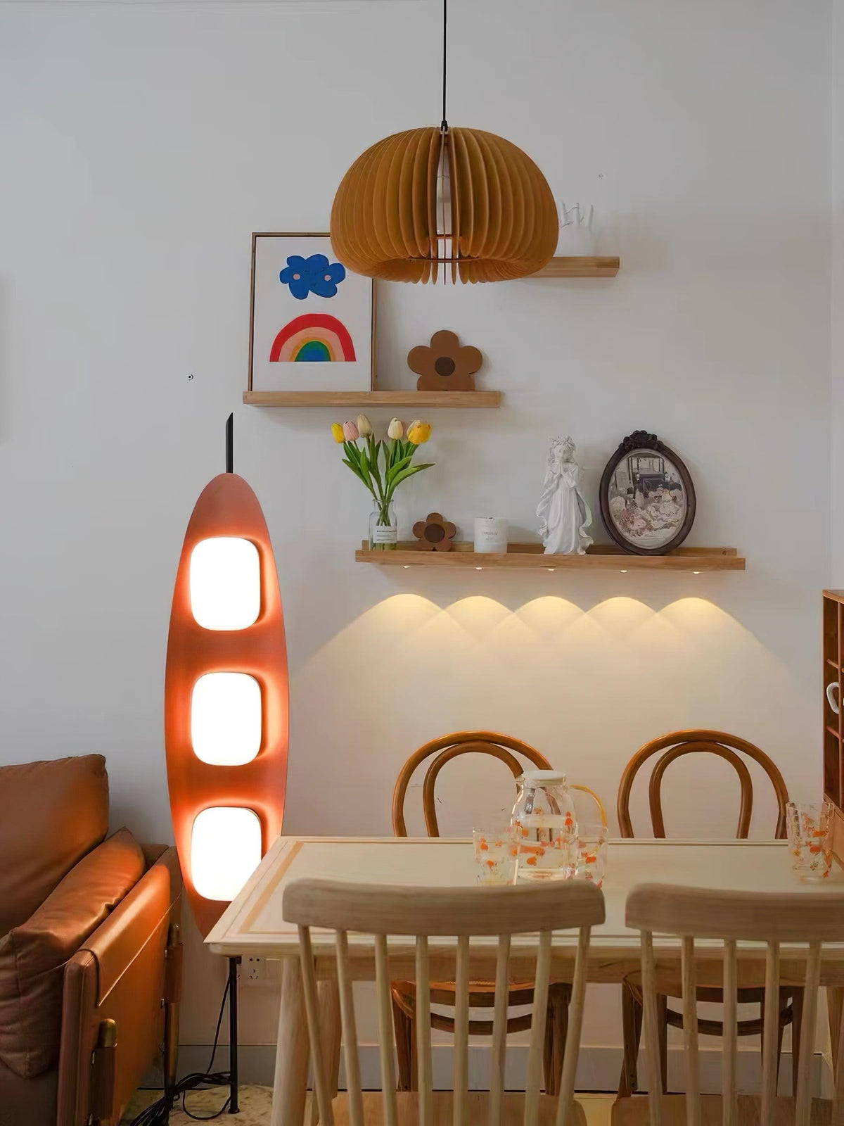 Clérachic teak floor lamp glowing near a wooden dining table, beneath a floating shelf and a folded paper pendant light.