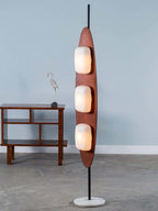 Clérachic teak floor lamp on its round marble base, photographed against a plain grey backdrop from a slightly different angle.