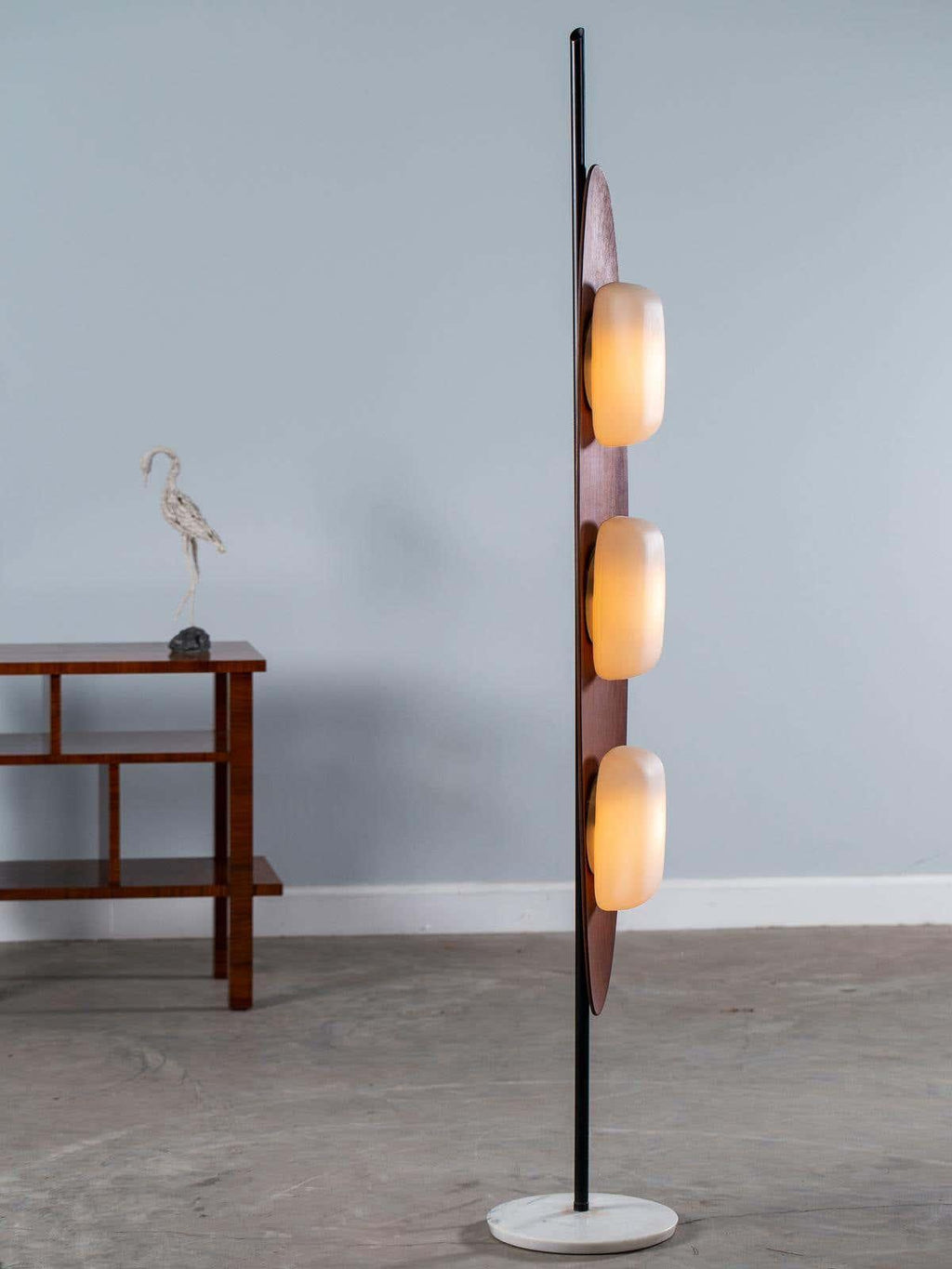 Clérachic teak floor lamp cropped closer against a plain grey backdrop, its three white glass shades softly glowing.