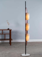 Clérachic teak floor lamp cropped closer against a plain grey backdrop, its three white glass shades softly glowing.