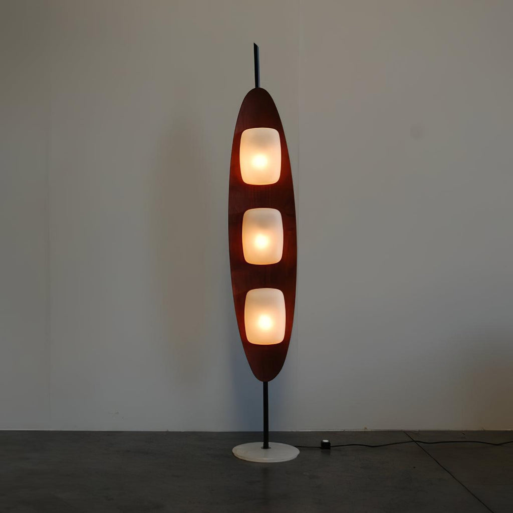 Clérachic teak floor lamp beside a wooden dining table, with houseplants and a city skyline visible through the window behind.