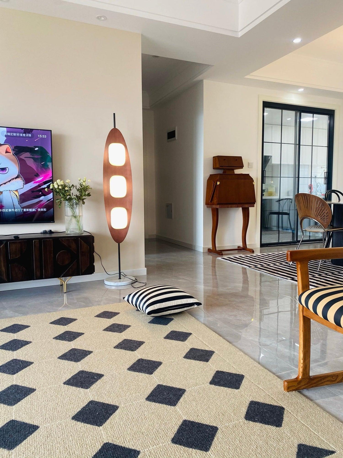 Clérachic teak floor lamp glowing in a living room with a black-and-white patterned rug, a striped floor cushion, and a TV stand.