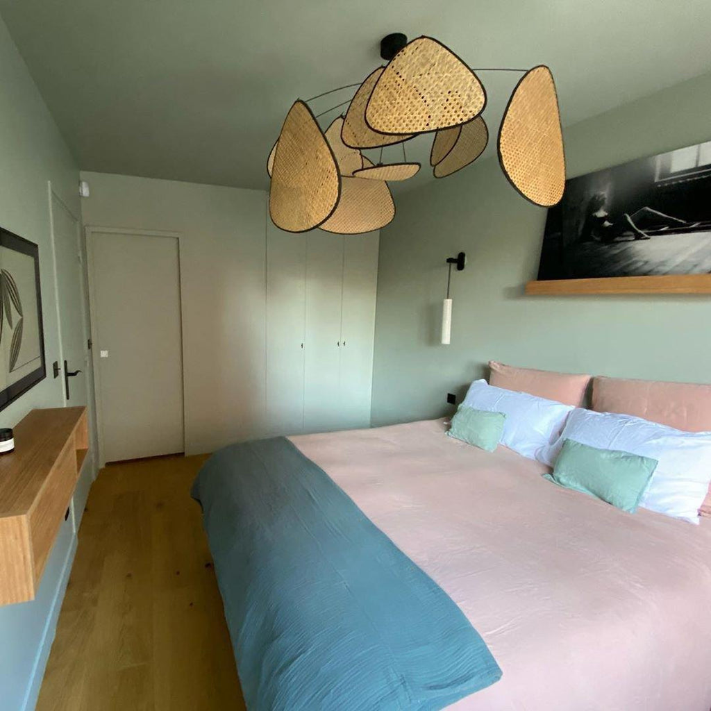This Clérachic pendant hangs in a sage-green bedroom, its black frame and paddles above pink and teal bedding.
