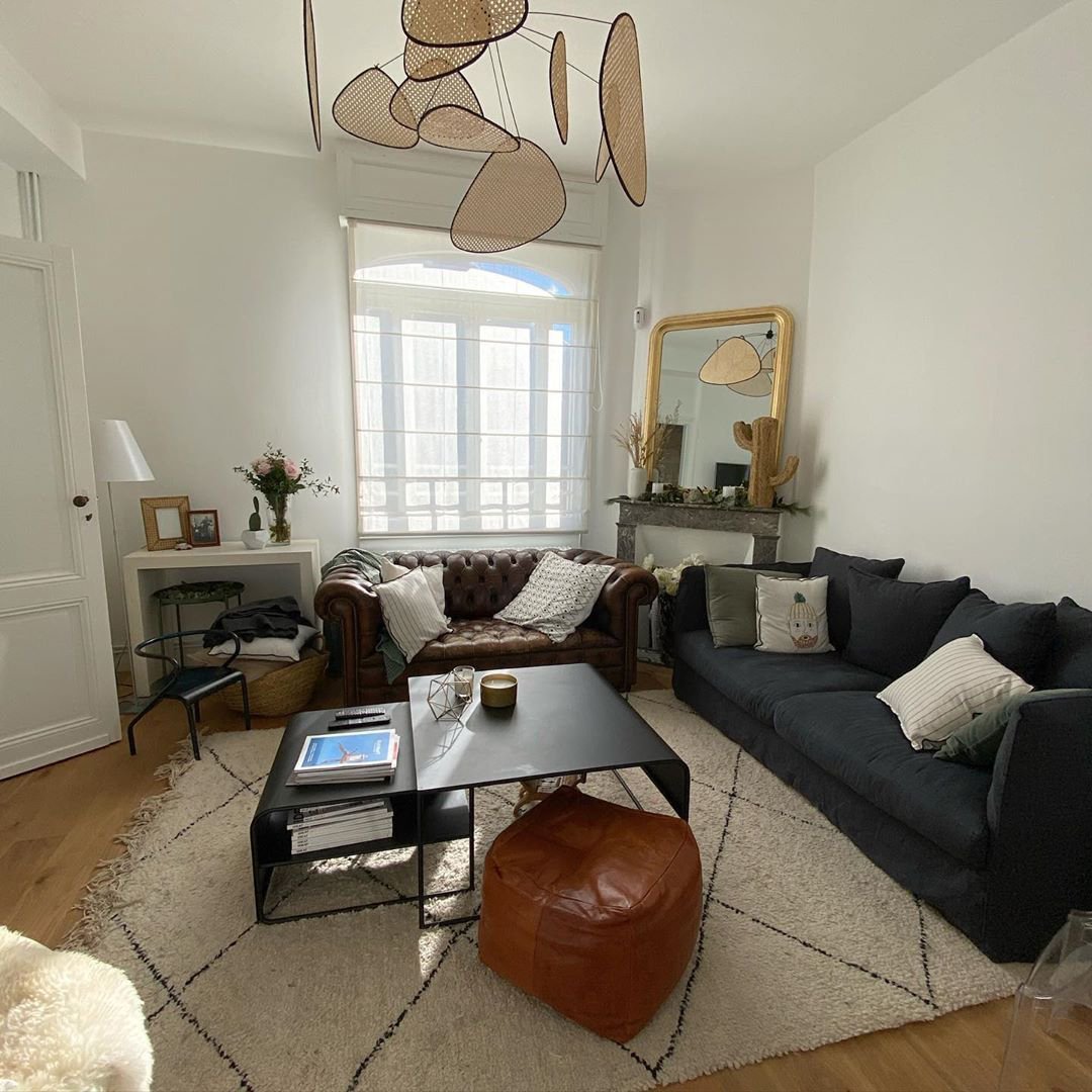 This Clérachic pendant hangs in a living room with a dark sofa, leather pouf and gilt-framed mirror.