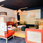 This Clérachic pendant hangs above an orange armchair and sheer curtain in a lounge with dark blue walls.