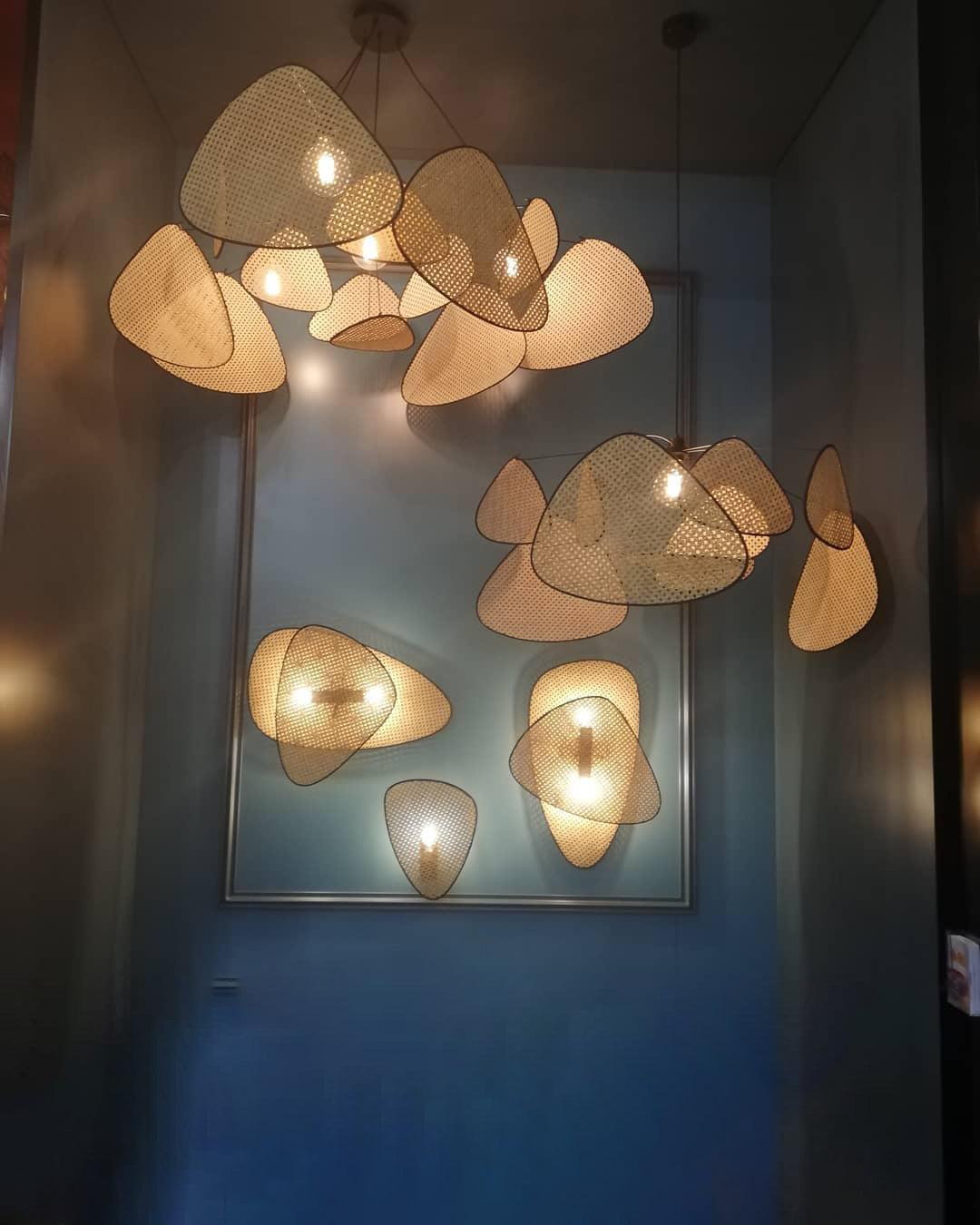 A display of woven rattan pendant lights from Clérachic hangs at different heights against a dark blue wall beside a leaning mirror.