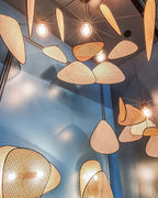 Several of this Clérachic pendant hang close together beneath a blue ceiling, their bamboo-weave paddles glowing around exposed bulbs.