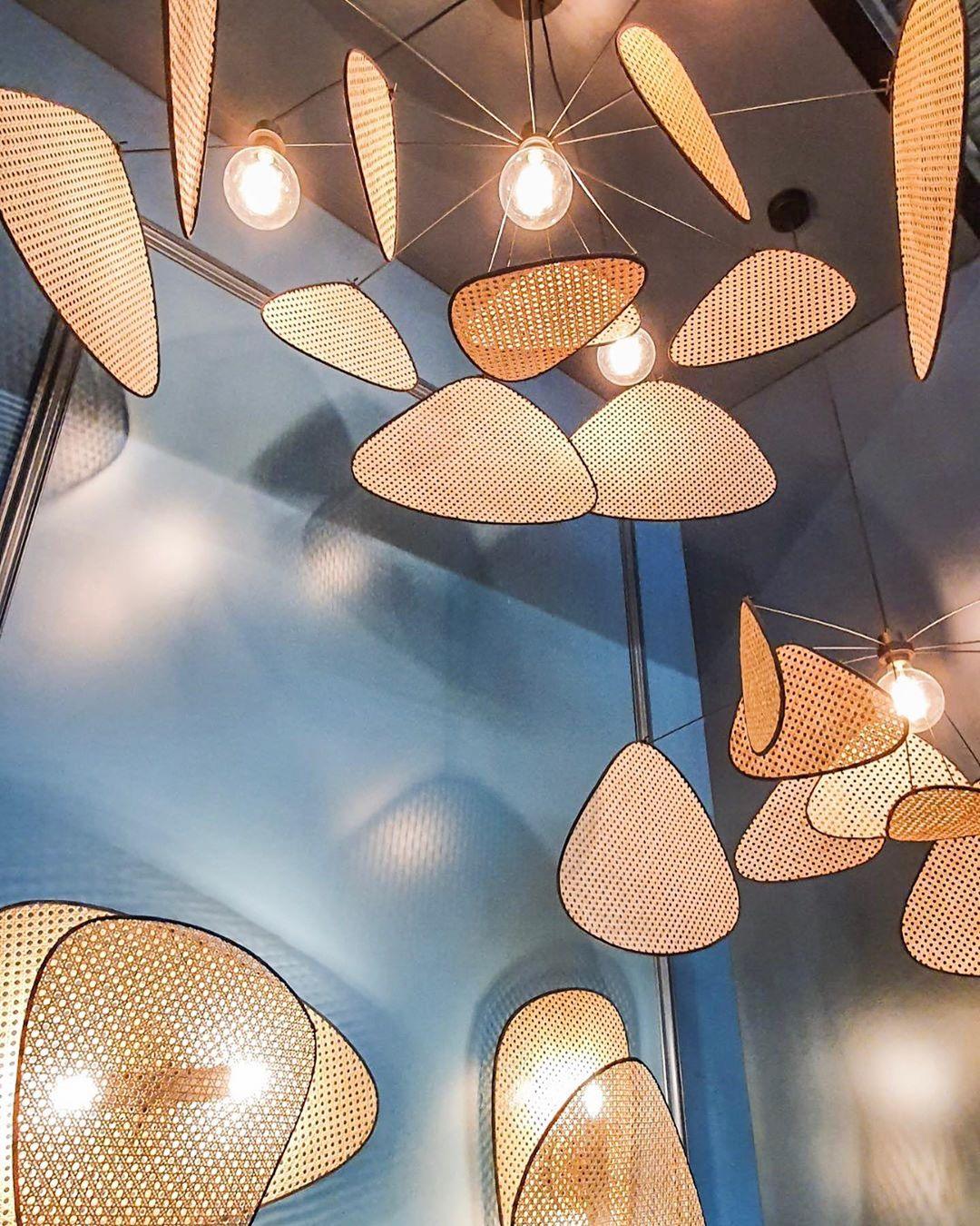 Several of this Clérachic pendant hang close together beneath a blue ceiling, their bamboo-weave paddles glowing around exposed bulbs.