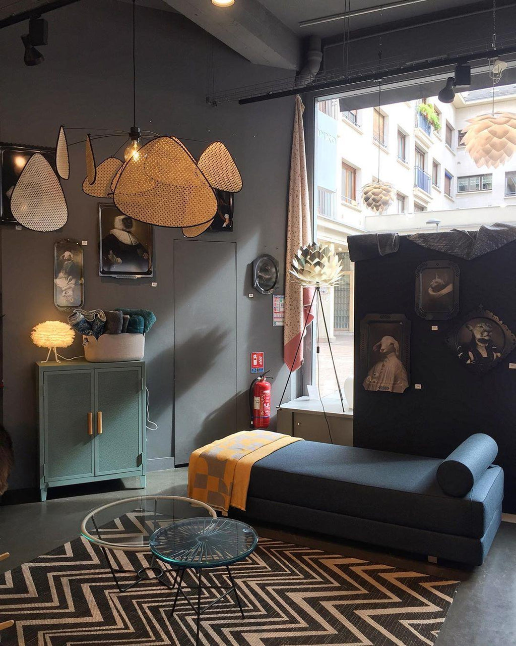 This Clérachic pendant hangs in the corner of a dark showroom furnished with a blue chaise and chevron-patterned rug.