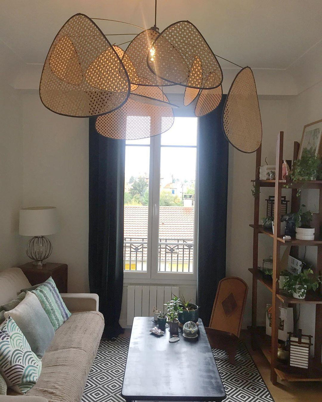 A grey sofa and coffee table sit beneath this Clérachic pendant in a living room with tall curtained windows.