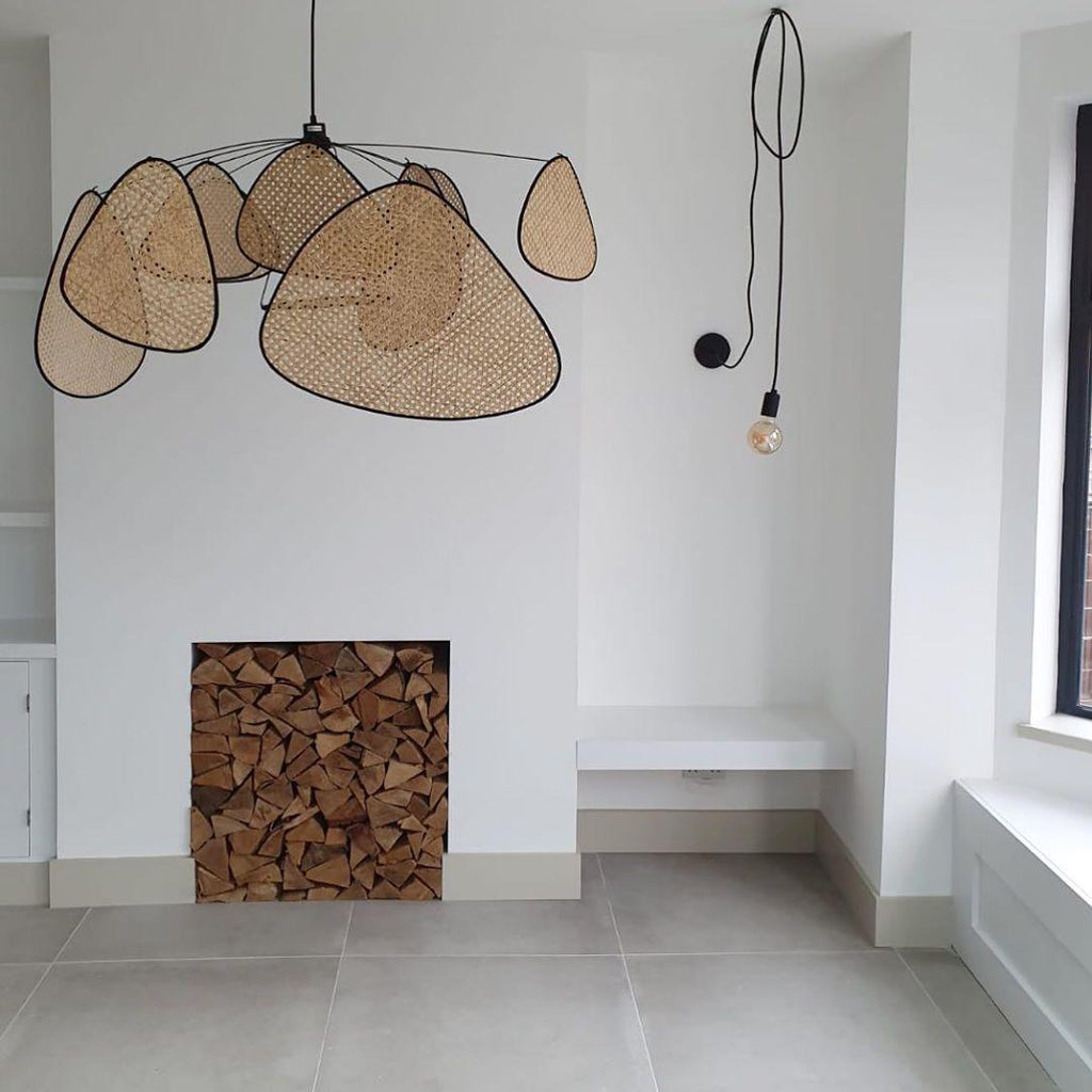 Beside a stacked firewood nook, this Clérachic pendant hangs in a bright white room with a wall-mounted bulb fixture.