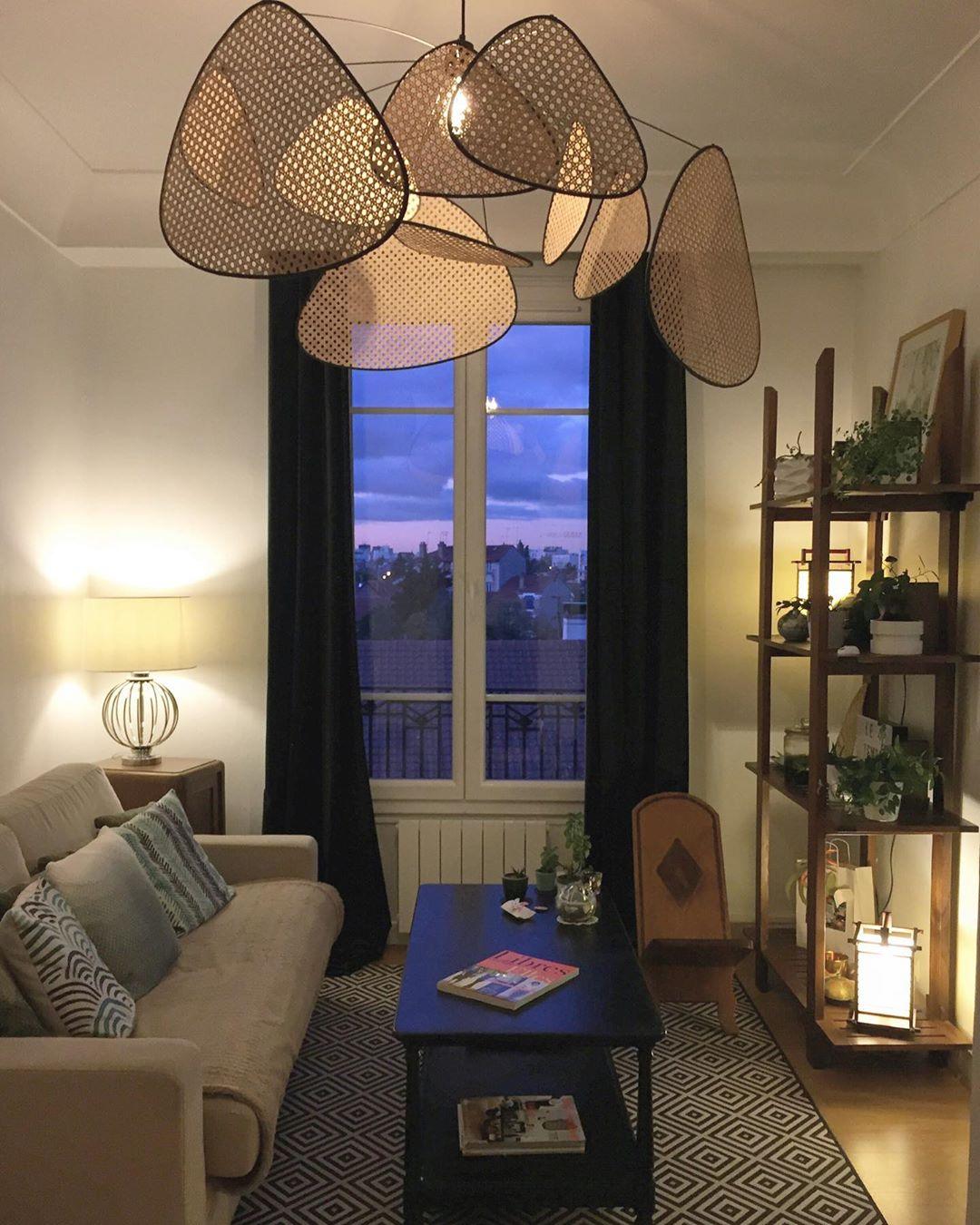 At dusk, this Clérachic pendant hangs above a blue sofa with city lights visible through the window behind.