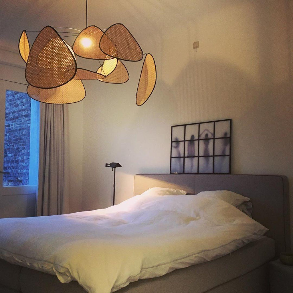 This Clérachic pendant hangs over a bed dressed in white linen, its black frame paddles beside a floor lamp.