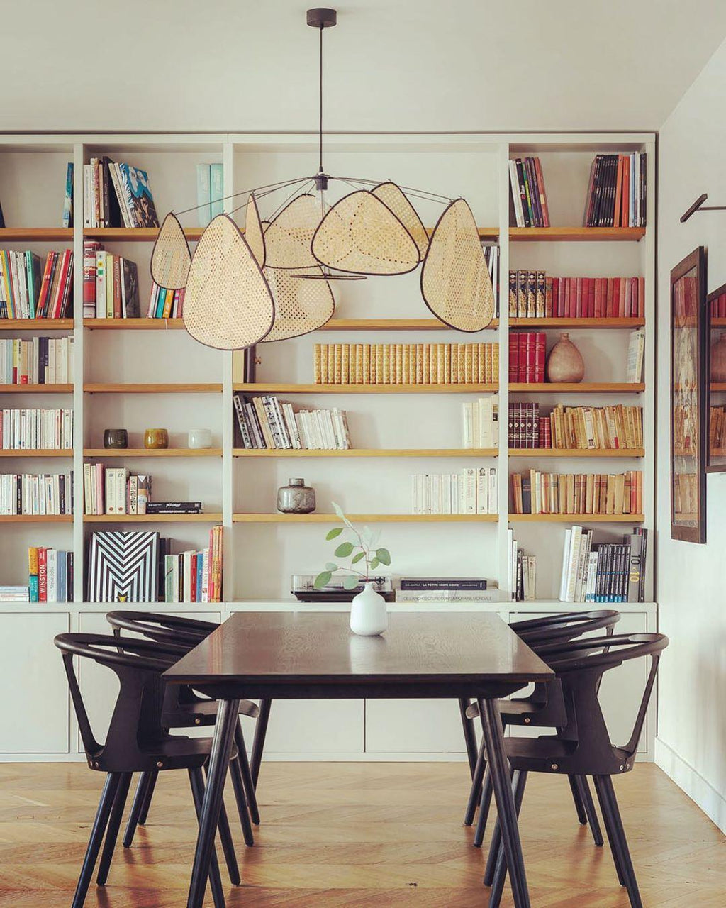 This Clérachic pendant hangs in front of floor-to-ceiling bookshelves above a dark dining table.