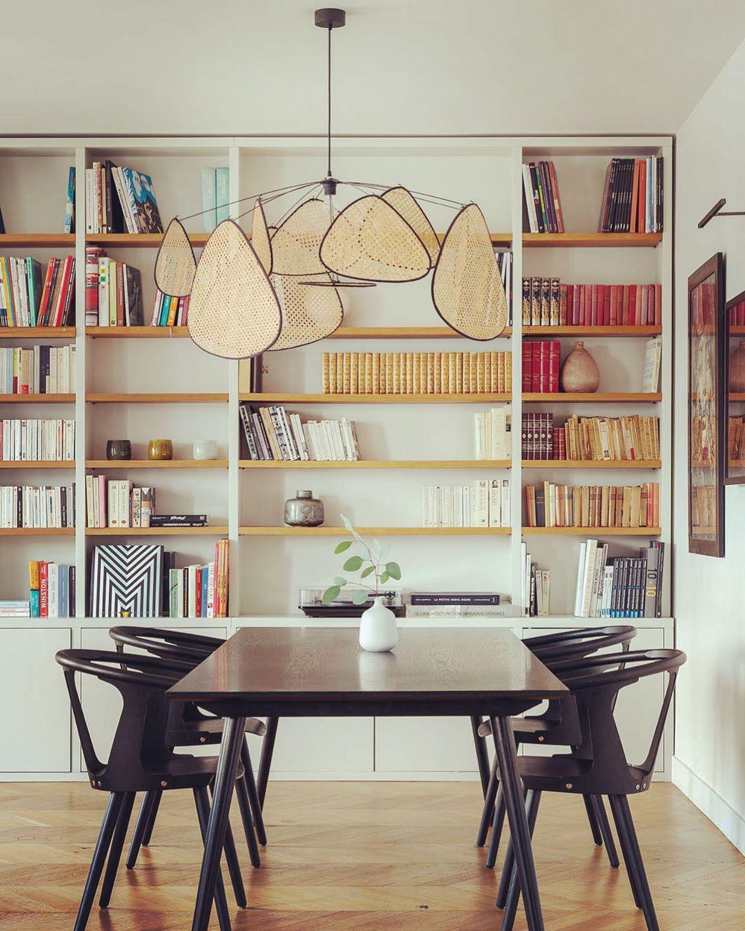 This Clérachic pendant hangs in front of floor-to-ceiling bookshelves above a dark dining table.