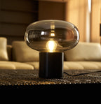 A close view of the Clérachic table lamp's dark marble base on a woven mat, with a cream sofa blurred in the room behind it.