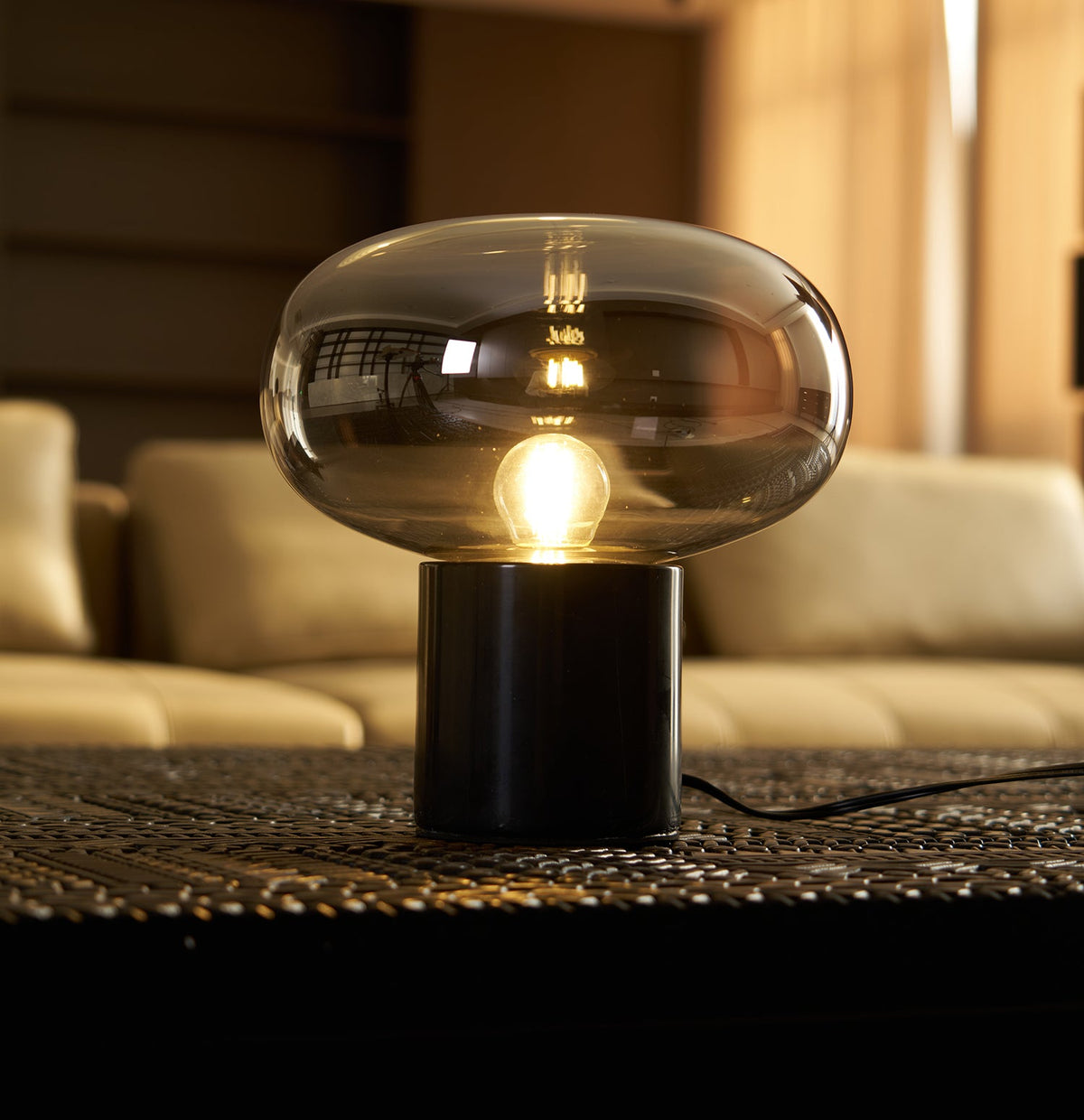 A close view of the Clérachic table lamp's dark marble base on a woven mat, with a cream sofa blurred in the room behind it.