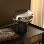 Close-up of the lit Clérachic table lamp beside the book Evero, the bulb's glow visible through the glass dome.