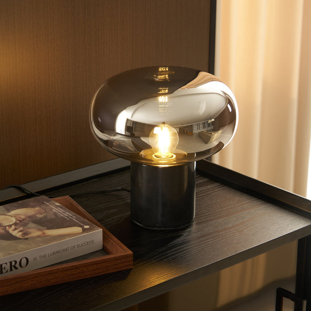 A side view of the Clérachic table lamp glowing on a dark console, the same book resting close to its marble base.