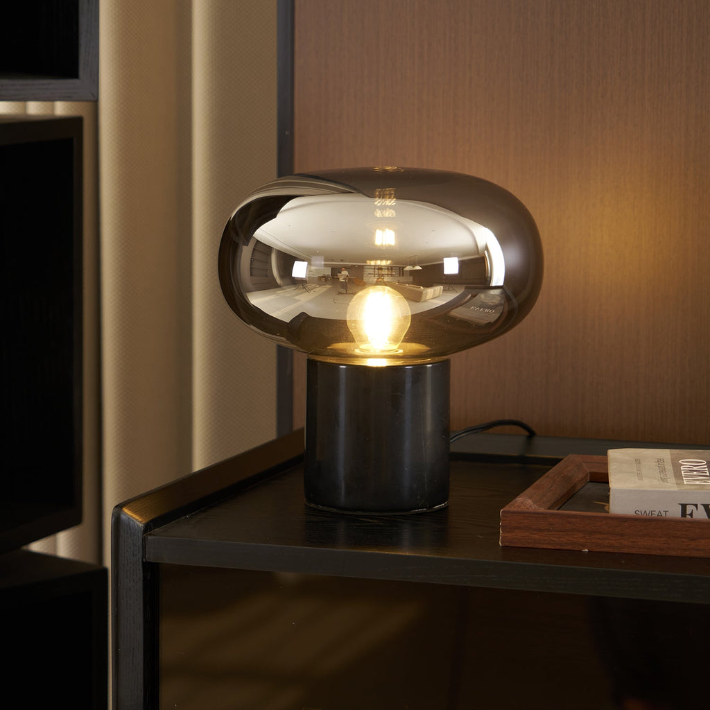 Another angle of the lit Clérachic table lamp on the same dark cabinet, the glass dome reflecting the room's warm light.