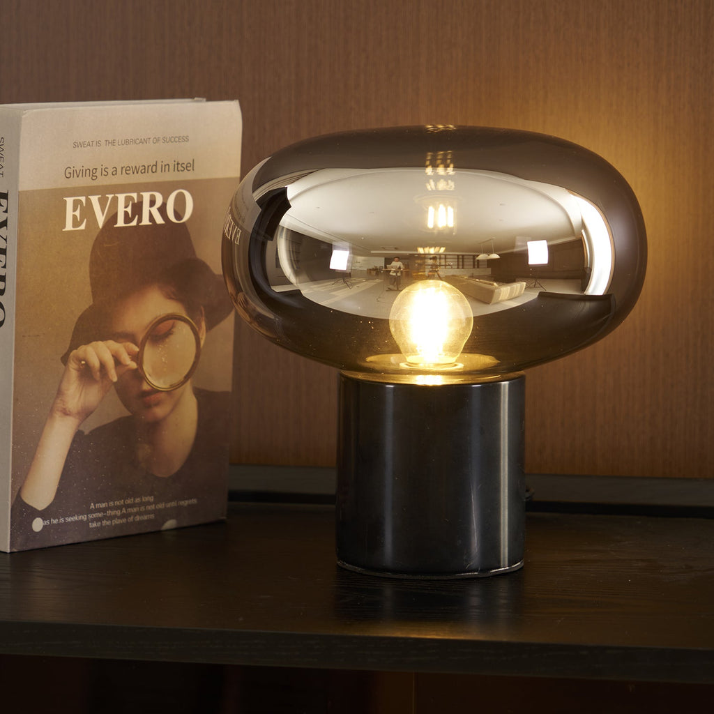 The lit Clérachic table lamp stands on a dark console table, positioned beside the book Evero propped upright nearby.