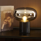 The lit Clérachic table lamp stands on a dark console table, positioned beside the book Evero propped upright nearby.