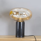 The lit amber-glass Clérachic table lamp on a wood table, its marble base set apart from the sunflowers in this crop.