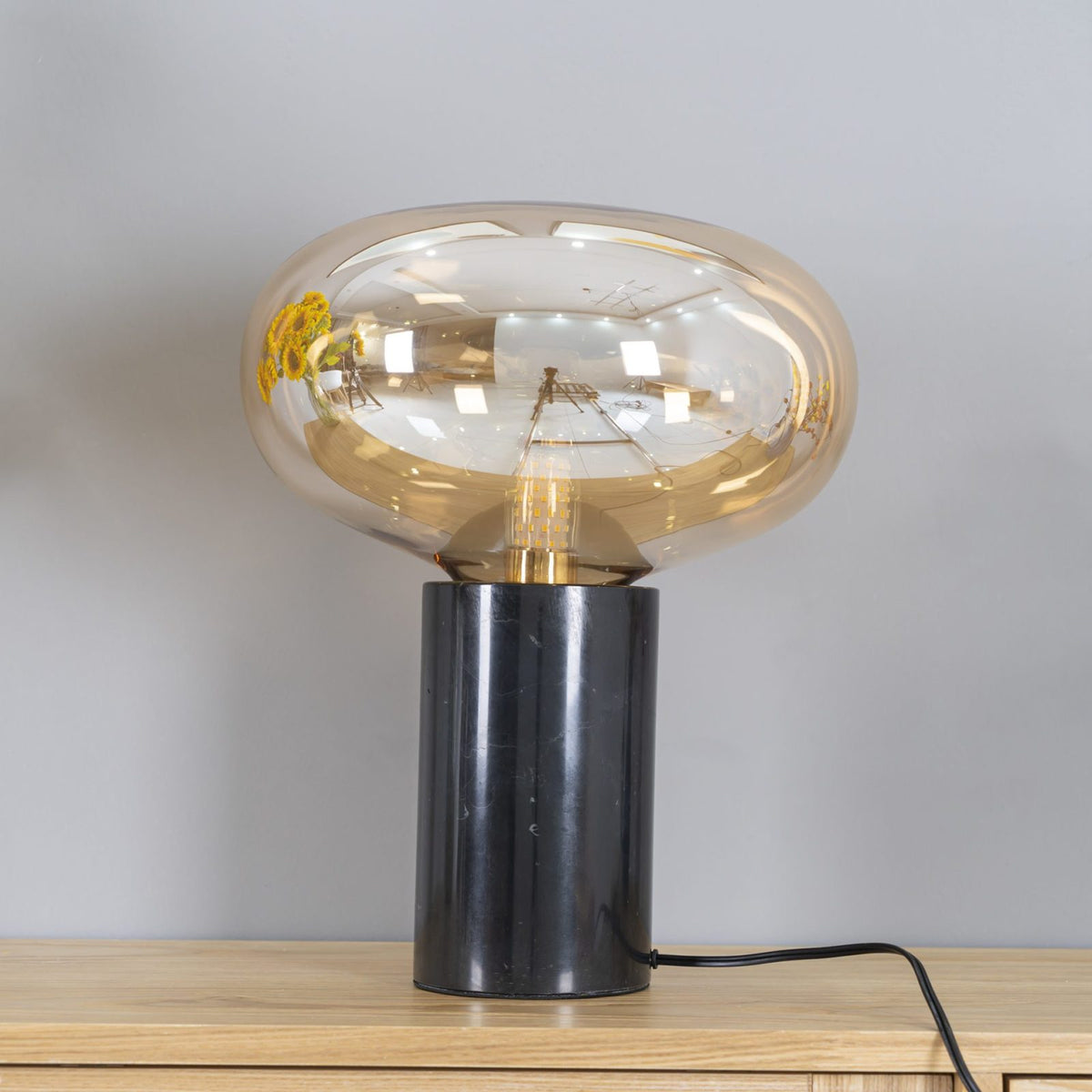 The lit amber-glass Clérachic table lamp on a wood table, its marble base set apart from the sunflowers in this crop.