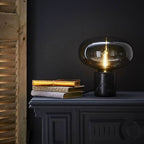 The lit amber-glass Clérachic table lamp on a dark mantel beside a stack of books, set against a near-black wall.
