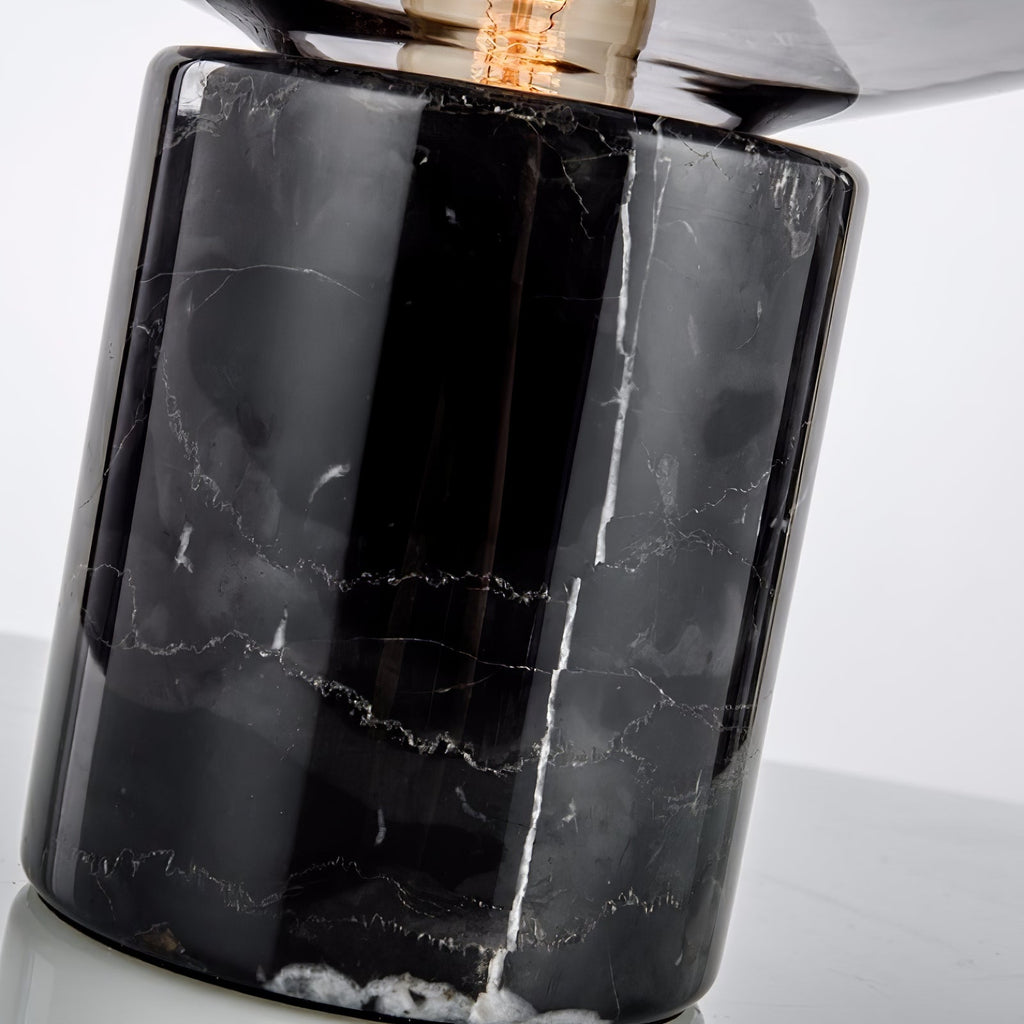 An extreme close-up of the Clérachic table lamp's black marble base, showing its natural veining beneath the glass dome.