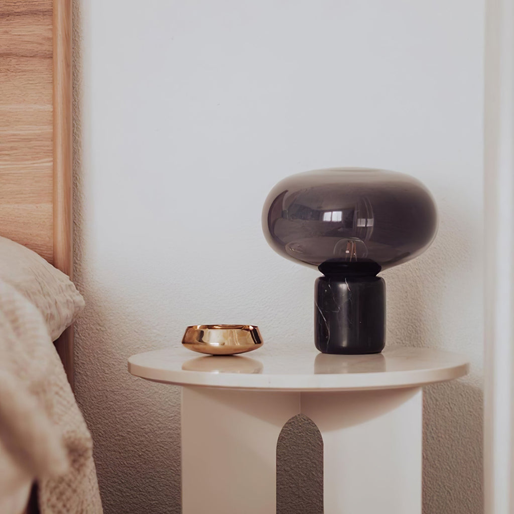 The Clérachic table lamp on a round nightstand beside a copper bowl, in a neutral-toned bedroom setting.