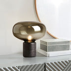 The amber-glass Clérachic table lamp on a white console table, beside a stack of shagreen boxes and a mirror.