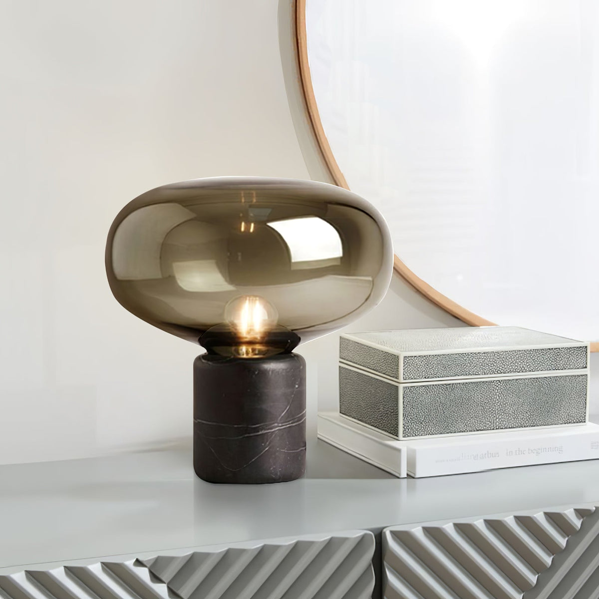 The amber-glass Clérachic table lamp on a white console table, beside a stack of shagreen boxes and a mirror.