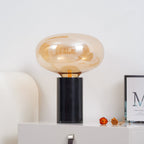 The amber-glass Clérachic table lamp on a white cabinet, with dried flowers and a framed print beside its black base.