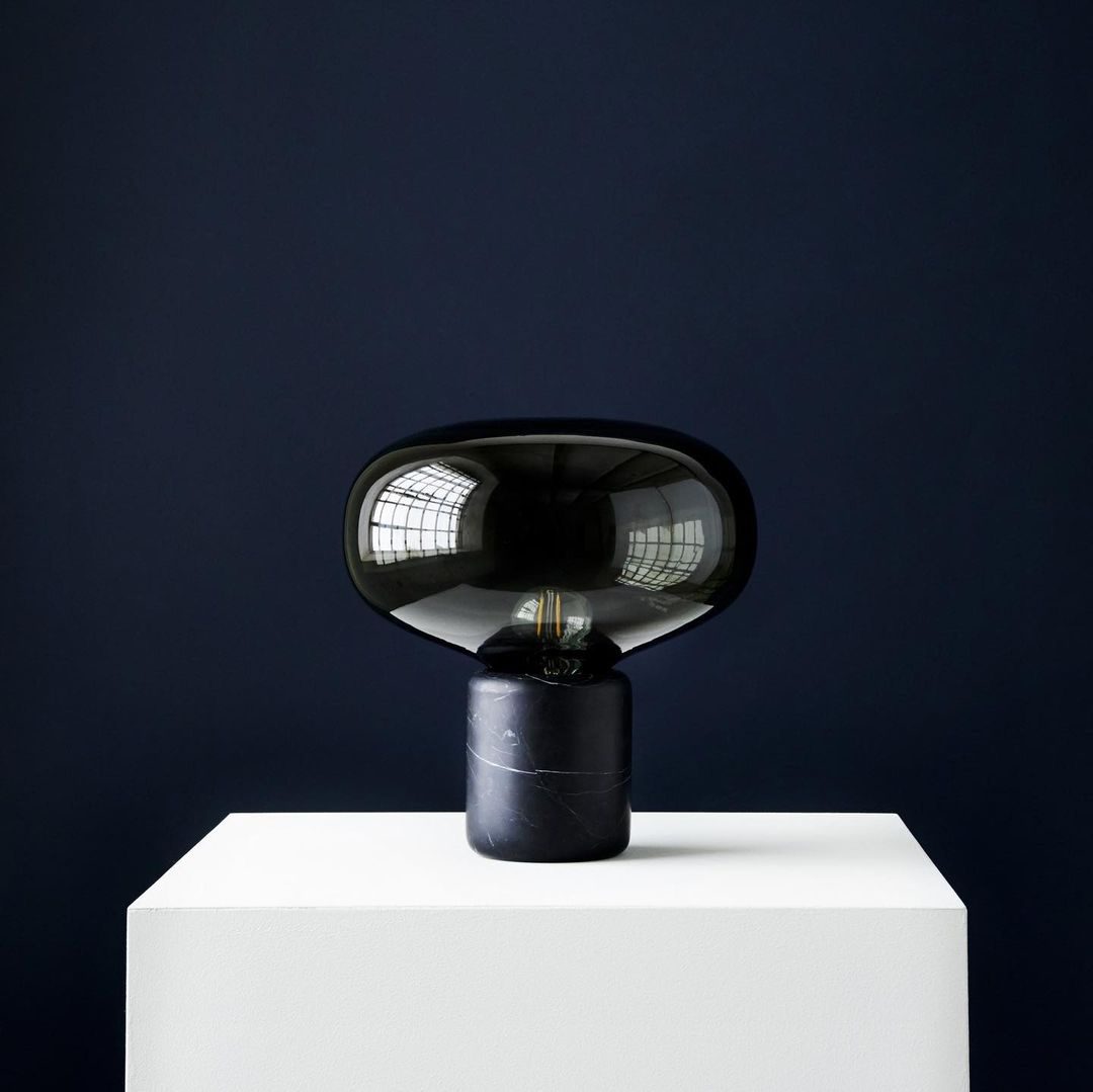 The Clérachic table lamp on a white plinth against a dark navy wall, its glass dome catching a single highlight.