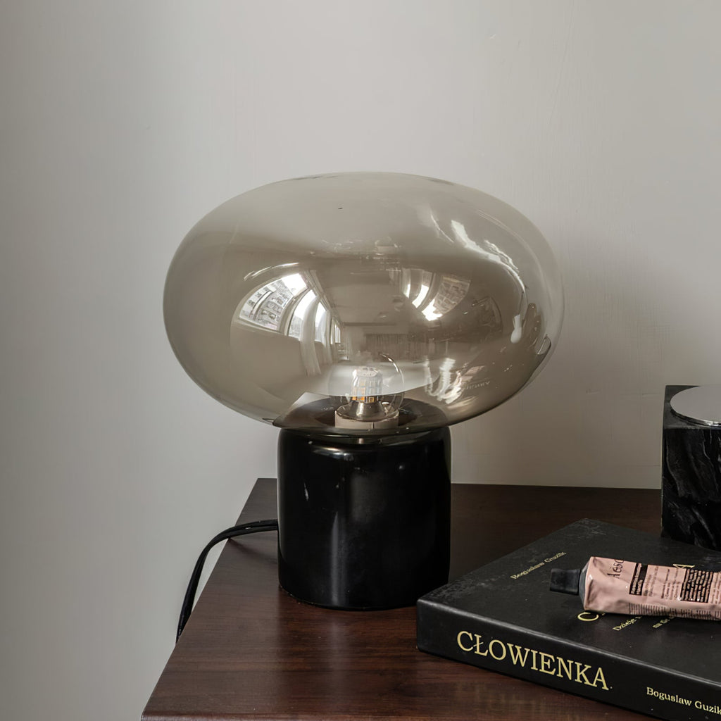 The Clérachic table lamp on a wood dresser beside a hardback book, its marble base grain visible beneath the dome.