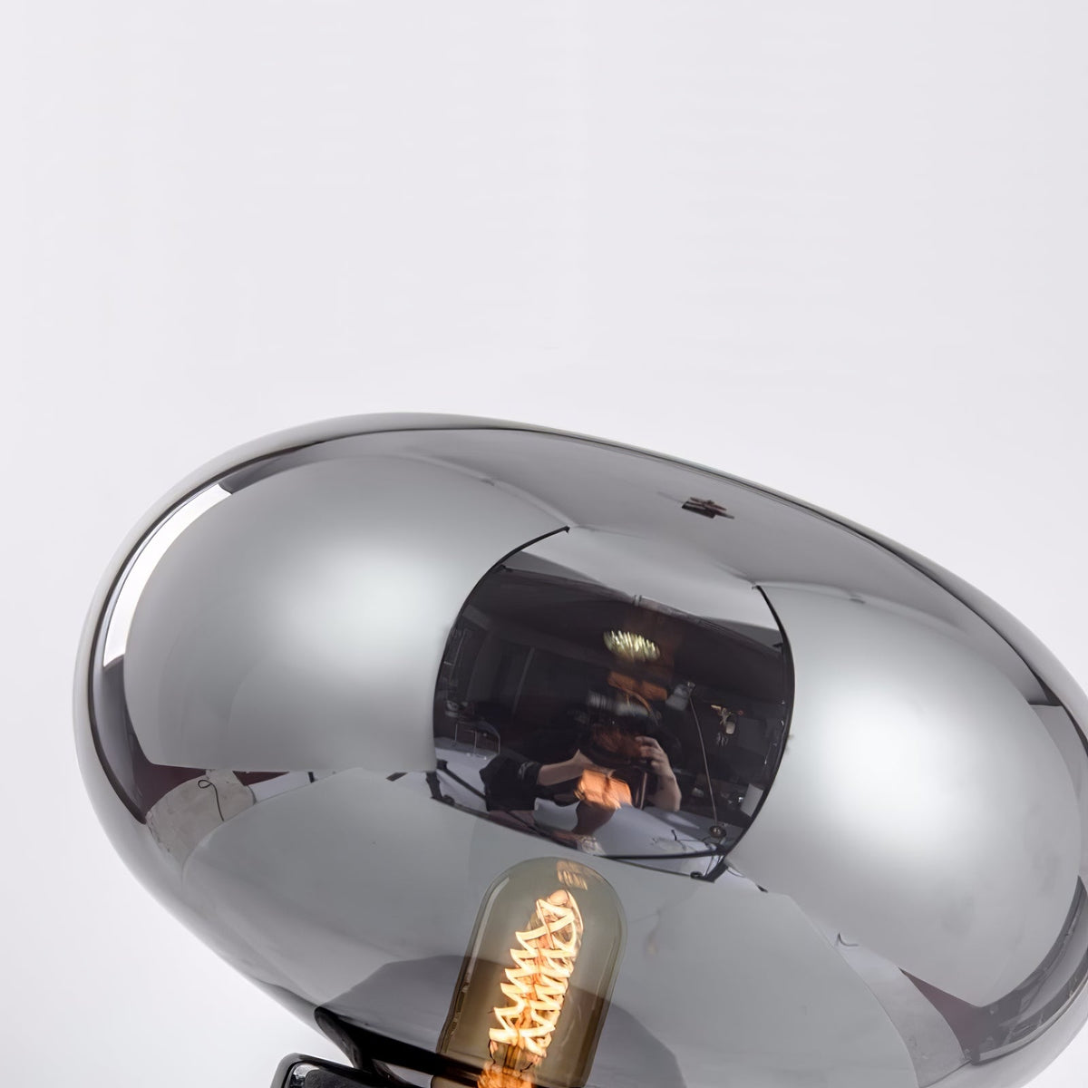 An extreme close-up of the Clérachic table lamp's glass dome, the filament bulb reflected across its mirrored surface.