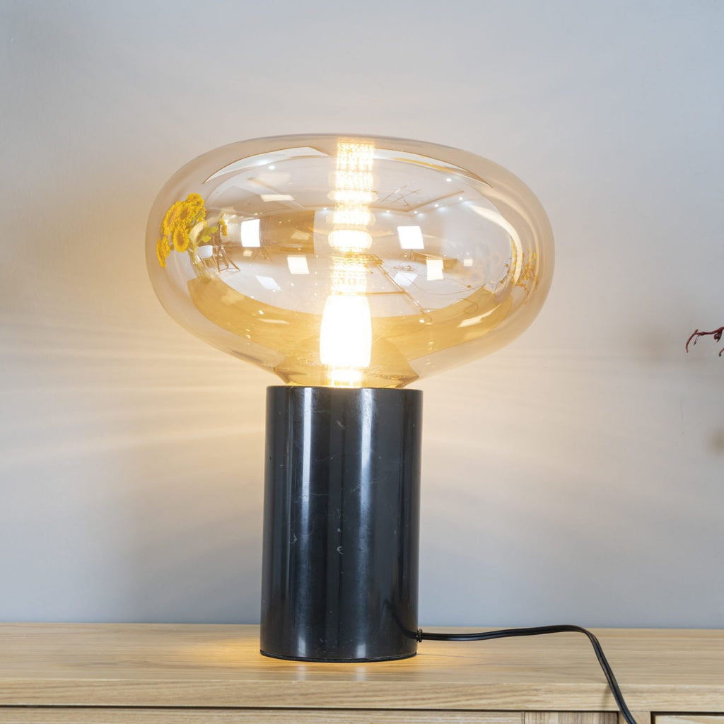 A closer angle of the lit amber-glass Clérachic table lamp beside sunflowers, showing the bulb through the dome.
