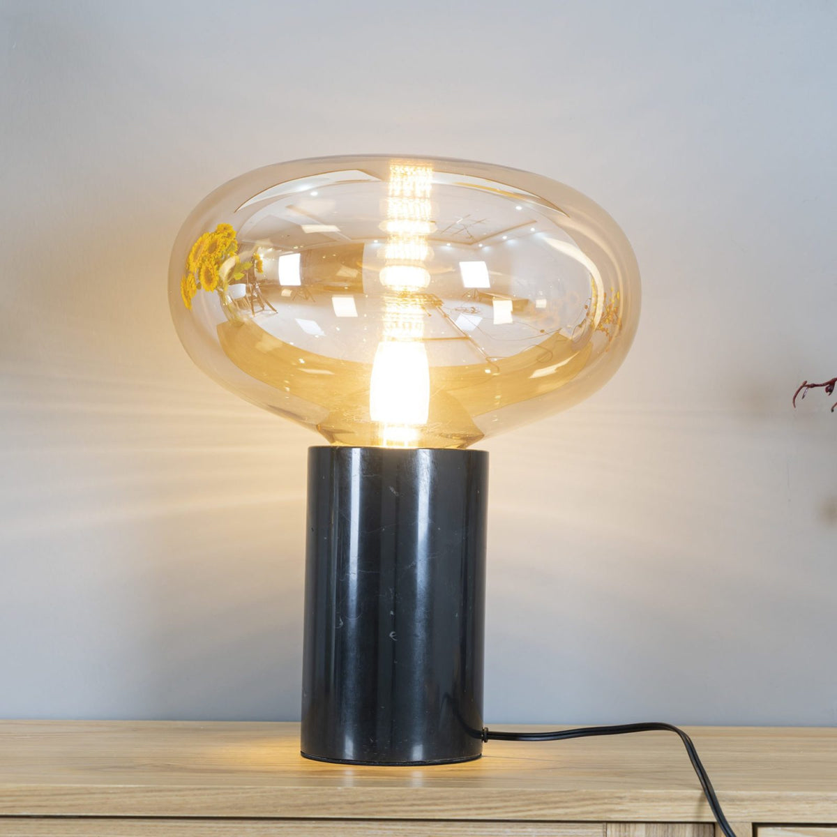 A closer angle of the lit amber-glass Clérachic table lamp beside sunflowers, showing the bulb through the dome.