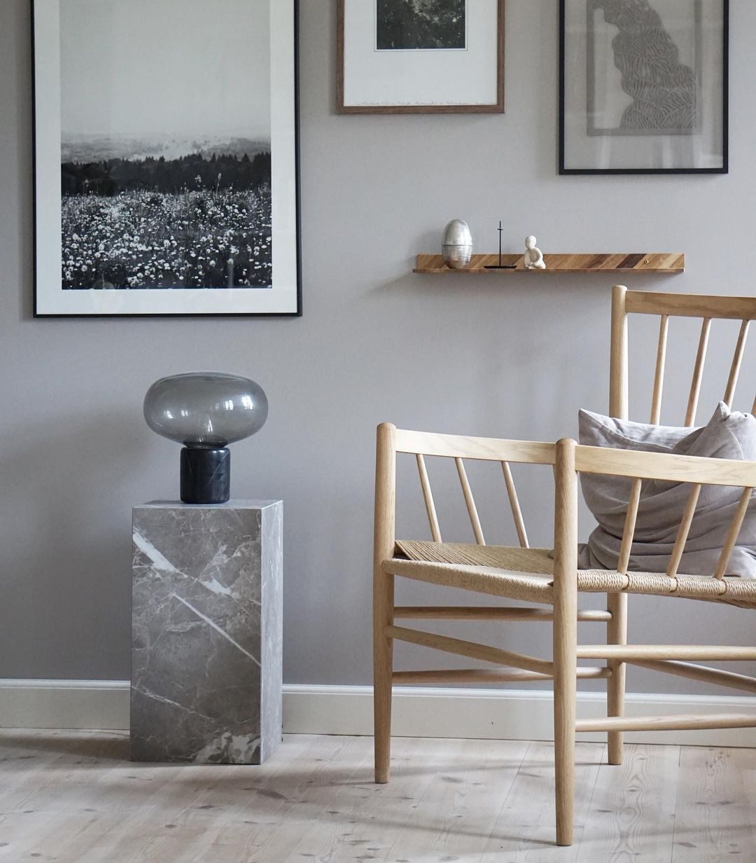 An unlit Clérachic table lamp on a grey stone pedestal, with wooden chairs and framed artwork in the room behind it.