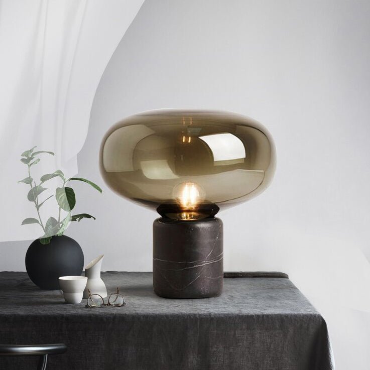 The Clérachic table lamp on a grey linen tablecloth beside a small black vase, a ceramic cup and folded glasses.