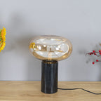 The lit amber-glass Clérachic table lamp on a wood table beside sunflowers and red berries in a softly lit room.