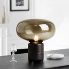 The Clérachic table lamp on a dark table beside a miniature glass lamp ornament and a small stack of plates.