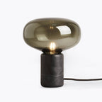 A straight-on studio view of the Clérachic table lamp on white, showing the marble base beneath the glass shade.